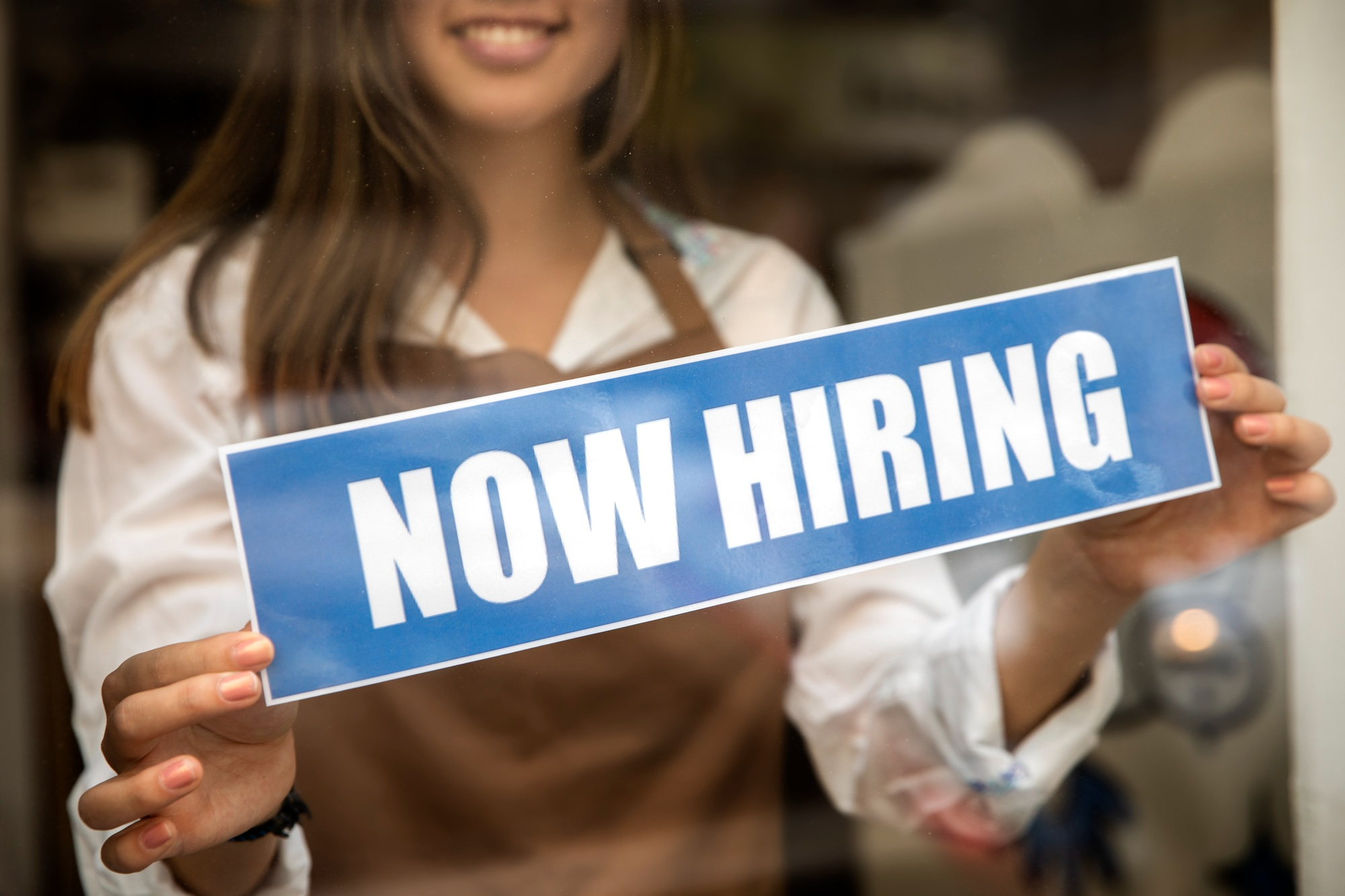 A store assistant sticking a "Now Hiring" sign | Source: Freepik